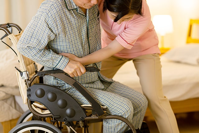 介護福祉士が利用者さんの身体を支えながら車椅子へ移動させている様子